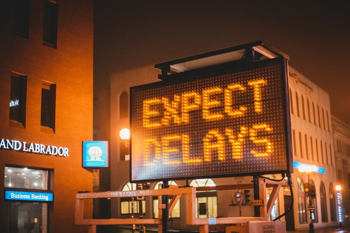 Letrero luminoso naranjo que dice EXPECT DELAYS en una calle de noche