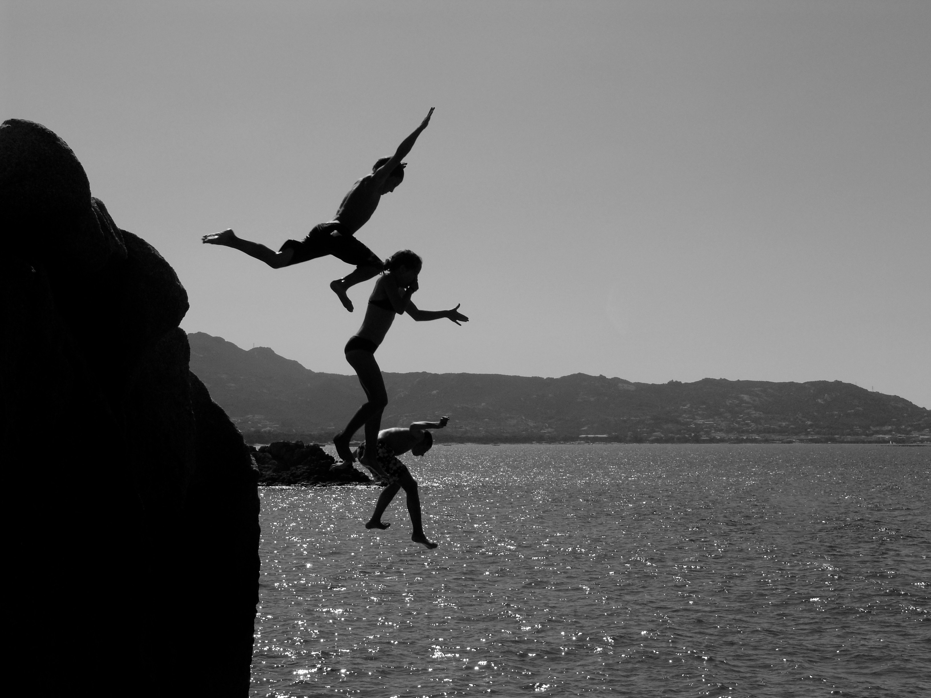 Tres personas saltando desde un acantilado hacia el mar, en blanco y negro