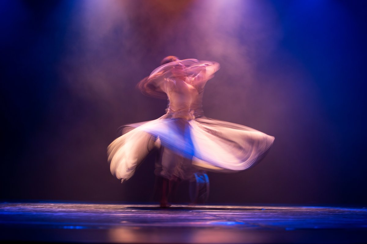 Bailarín girando envuelto en tela blanca sobre un escenario con luces azules y púrpuras