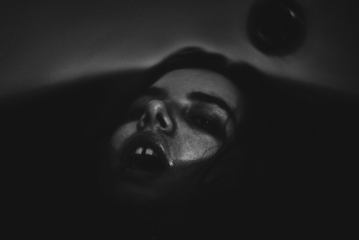 Primer plano en blanco y negro de un rostro en penumbra, con la boca entreabierta y un hilo de humedad en la mejilla