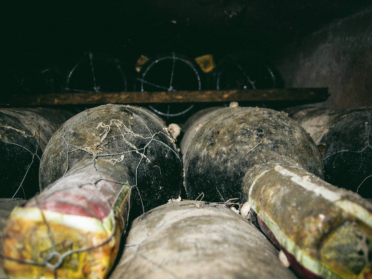 Botellas de vino cubiertas de polvo y telarañas apiladas en una bodega oscura