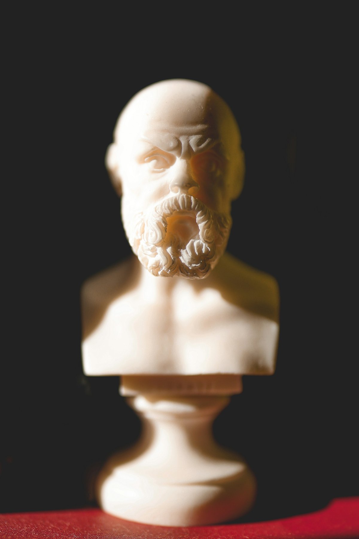 Busto de mármol de un filósofo griego iluminado con luz cálida contra un fondo oscuro
