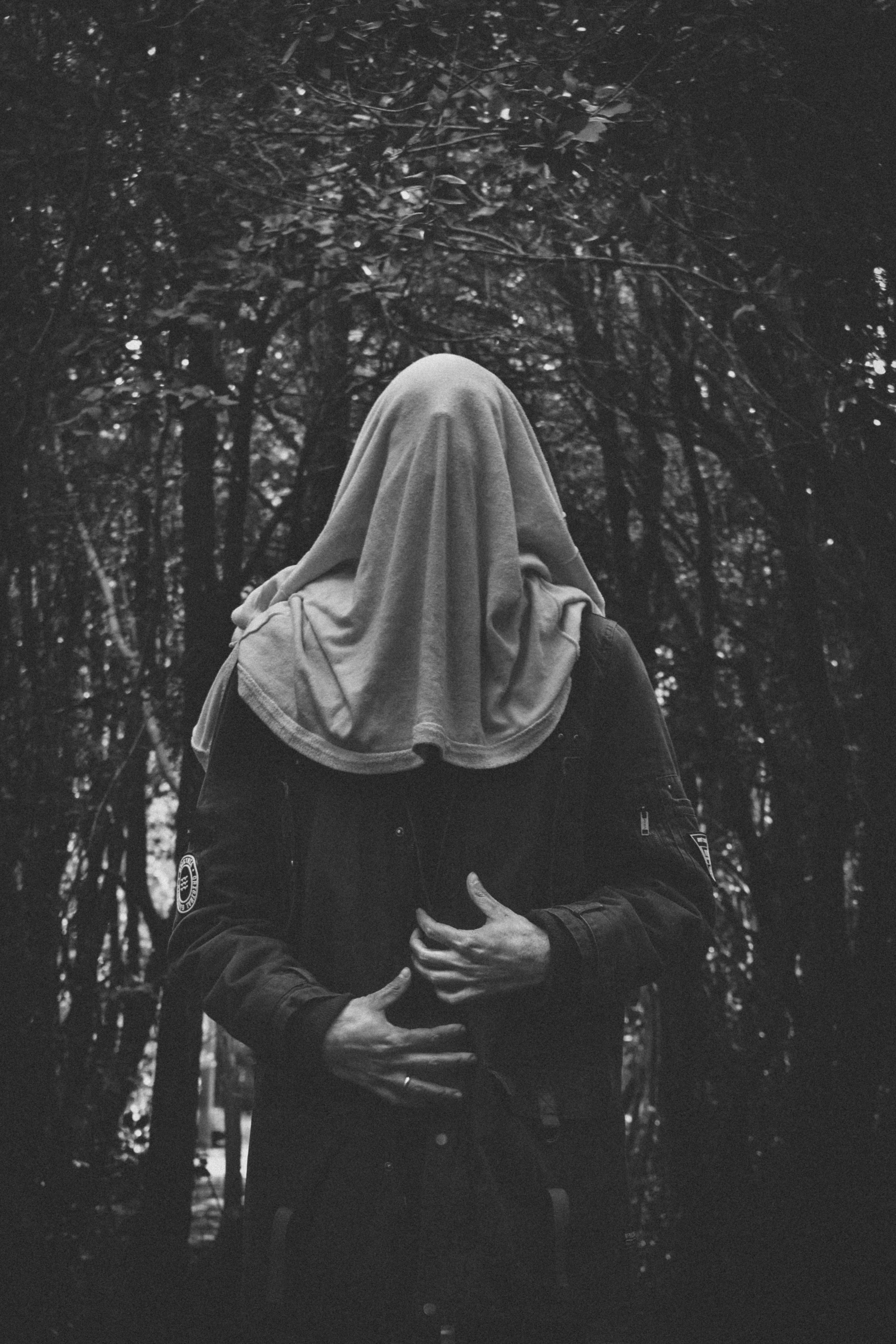 Figura encapuchada de espaldas en un bosque oscuro, con las manos entrelazadas al frente
