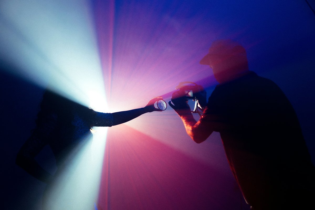 Silueta de una persona sosteniendo una cámara antigua entre haces de luz azul y magenta